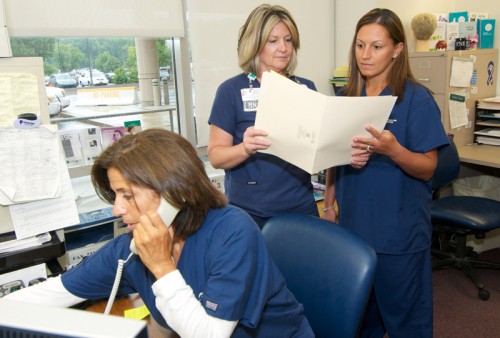 Forensic nurse examiners Erica Dempsey, RN III, and Christi Mench, RN, review a patient's chart at shift change at Christiana Hospital Emergency Department. In the foreground is Dee Lougheed, RN, FNE.