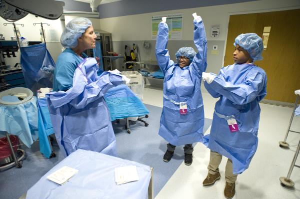 Beth Fitzgerald, RN, MSN, CNOR, perioperative simulation specialist, teaches students how to “gown and glove” during a Prestige Academy Charter School tour of Christiana Hospital.