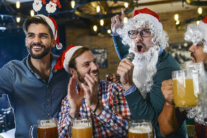 Group of friends wearing holiday hats drinking beer and acting jolly.