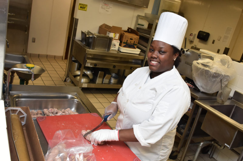 William Penn High School senior Tiabronna Cooper prepares sweet Italian sausage for supper on at the high-volume West End Cafe, Christiana Hospital.