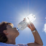 Woman, senior, drinking water in the sunlight, back lit image with sunbeams.