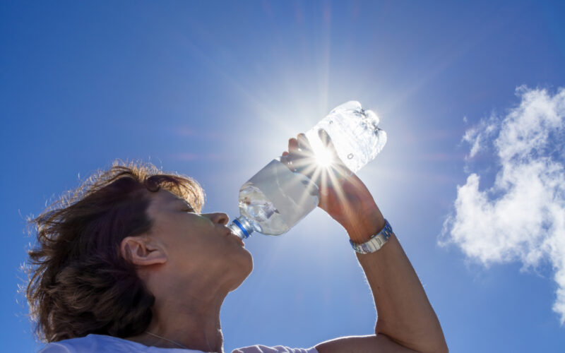 Woman, senior, drinking water in the sunlight, back lit image with sunbeams.